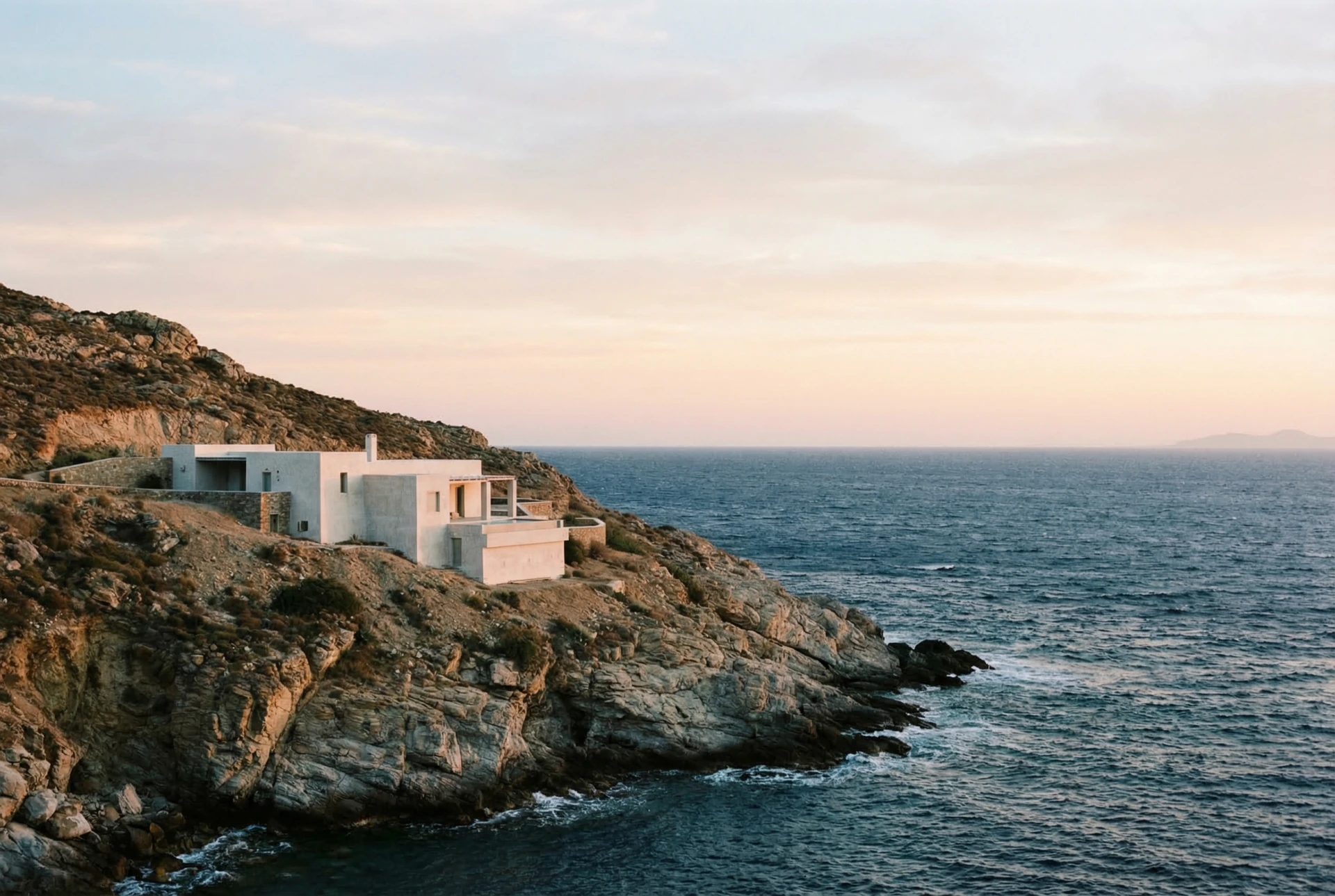 Minimalist white villa on Greek cliffside overlooking the Aegean at dawn